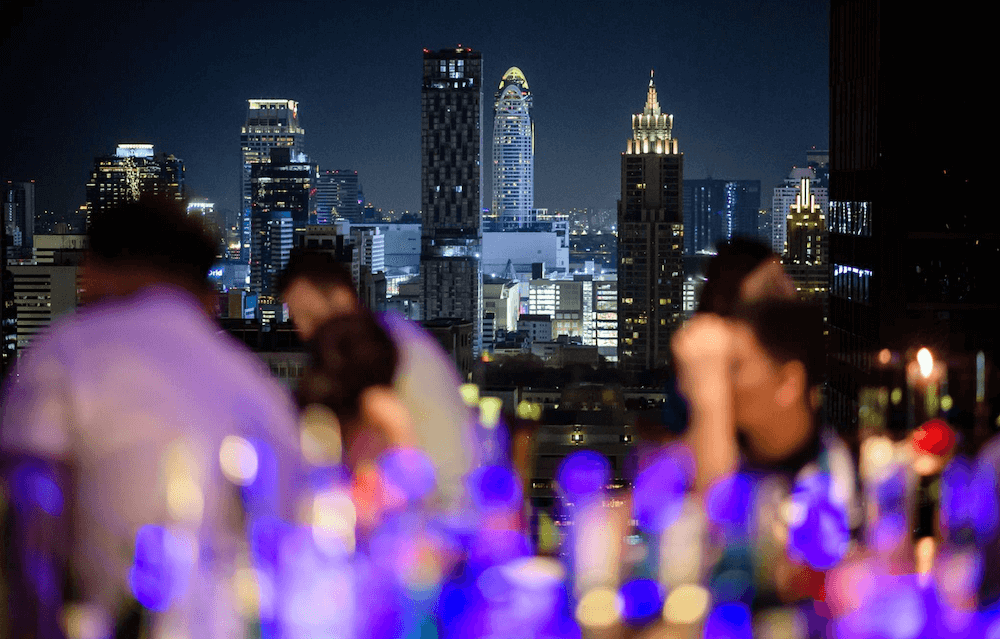 people in a bar blurred with focus on bangkok city skyscrapers