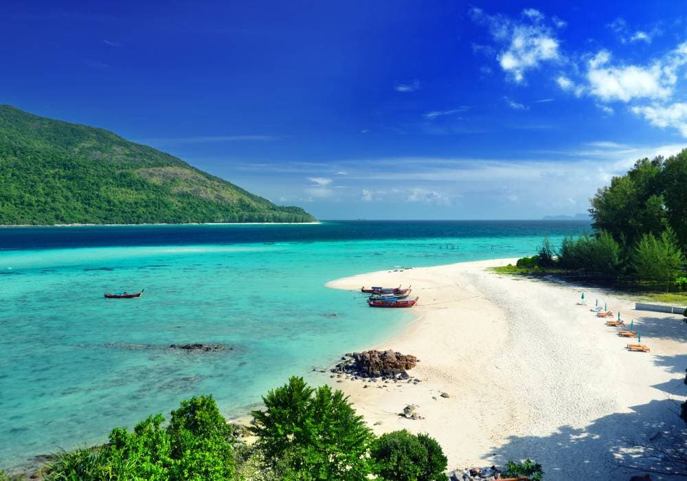 koh lipe white and with bright blue water and darker blue water green hills in background