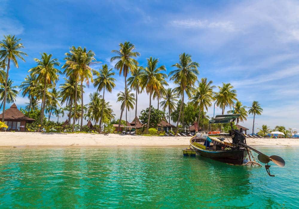 koh mook palm trees and small hurts lined on the beach against turqouise water
